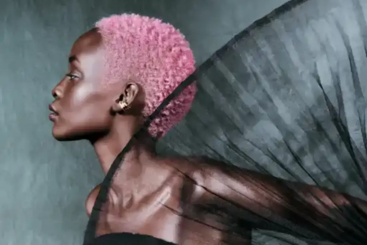 Profile view of a person with short pink hair and dark skin, wearing a sheer black fabric draped over their shoulder against a gray background, evoking a sense of wellbeing and modern wellness-rituals. - Jax Salon and Spa