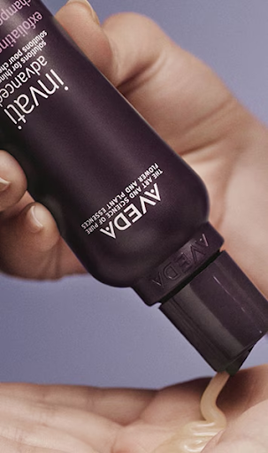 A person dispenses a cream from a purple Aveda Invati Advanced bottle onto their hand. - Jax Salon and Spa