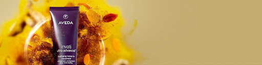 Aveda Invati Advanced bottle is displayed against a yellow and orange floral background on a beige surface, perfect for winter hair care and holiday hair prep. - Jax Salon and Spa