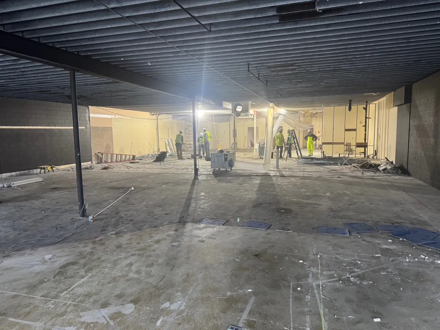 IMG_4591 Construction workers in safety gear stand inside a large, partially finished building with exposed ceiling and scattered equipment and materials. - Jax Salon and Spa
