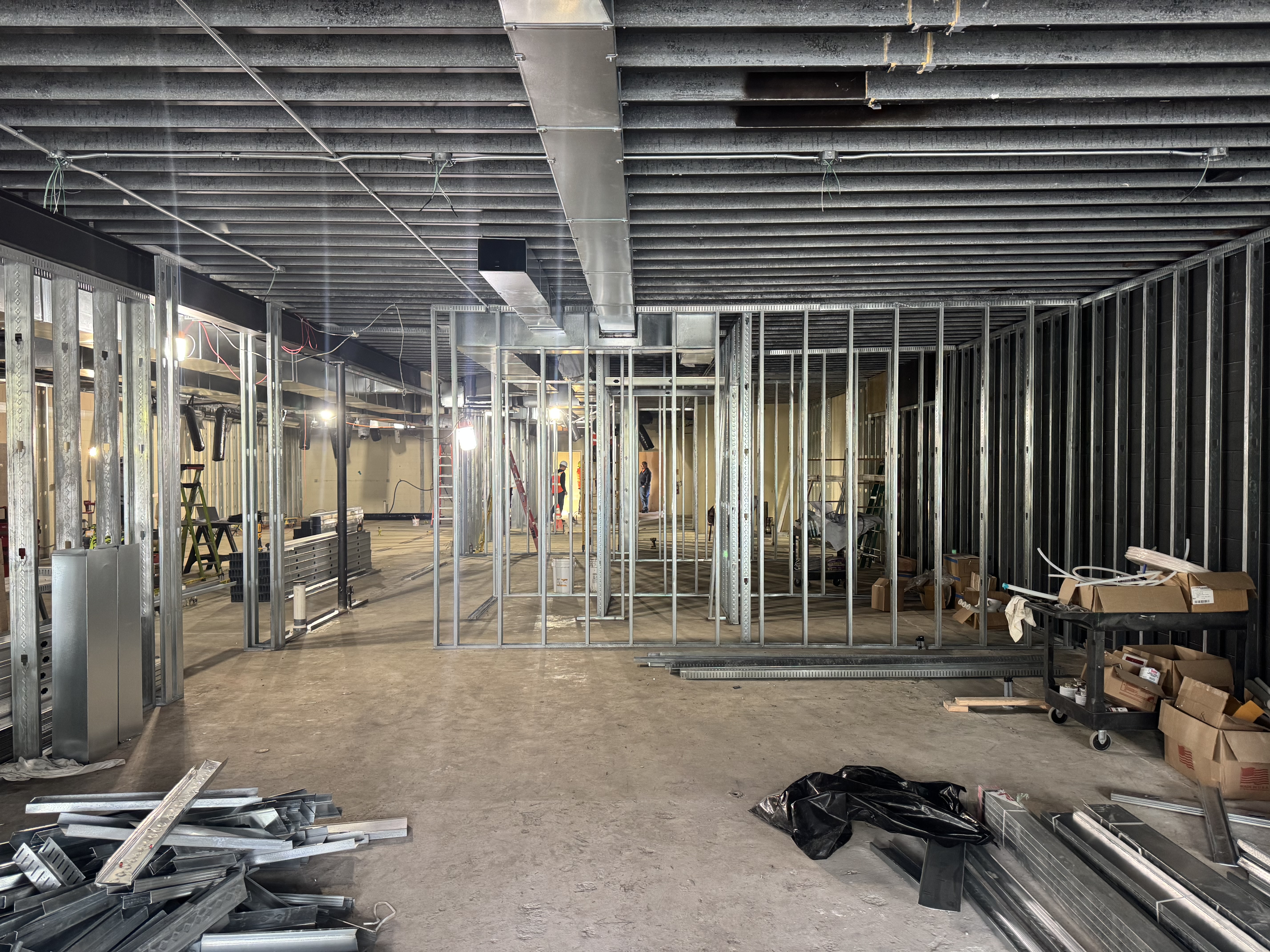 Interior view of a building under construction with exposed metal wall framing, construction materials, and tools scattered on the unfinished concrete floor. - Jax Salon and Spa