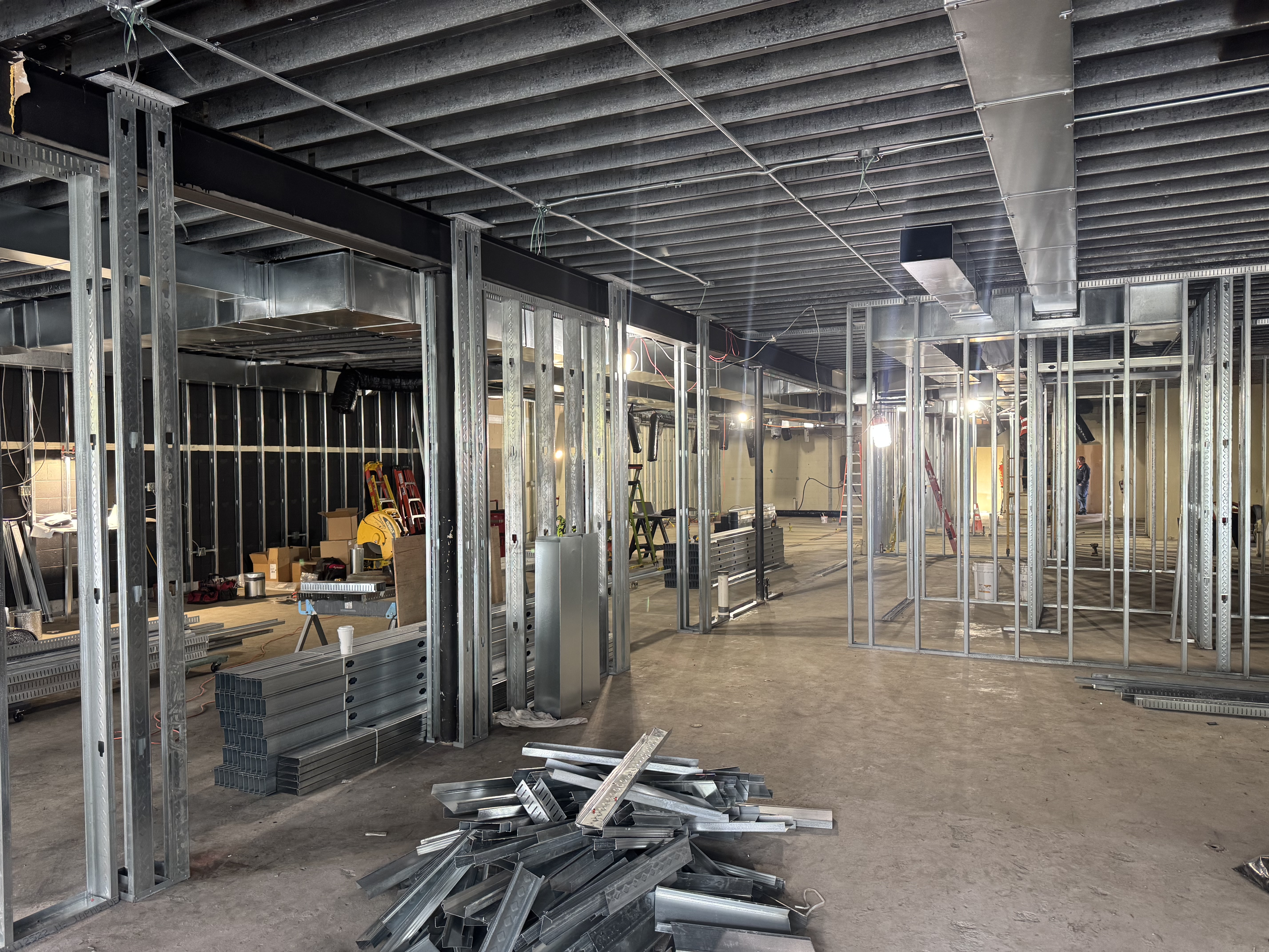 Interior view of a building under construction, showing exposed steel framing, unfinished ceilings, tools, and construction materials scattered on the floor. - Jax Salon and Spa