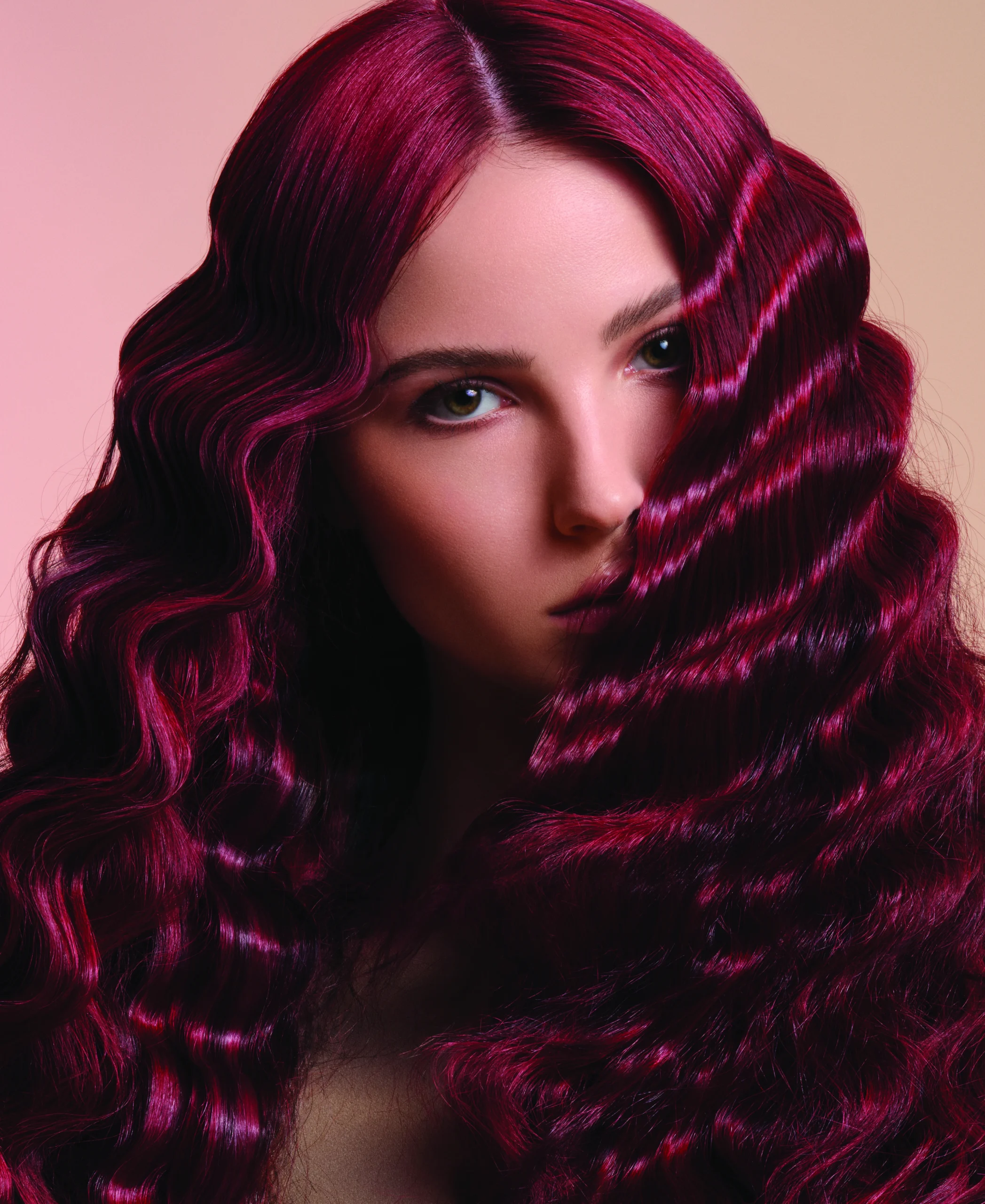Woman with long, deep burgundy wavy hair, styled in defined waves, looking directly at the camera against a neutral background. - Jax Salon and Spa