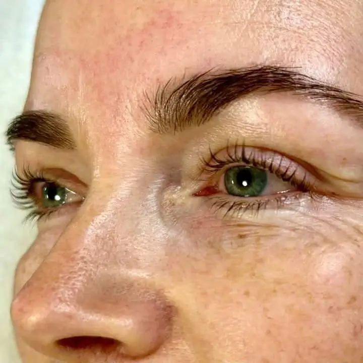 Close-up of a person's face showing green eyes, dark eyebrows, long eyelashes, visible pores, and fine lines around the eyes. - Jax Salon and Spa