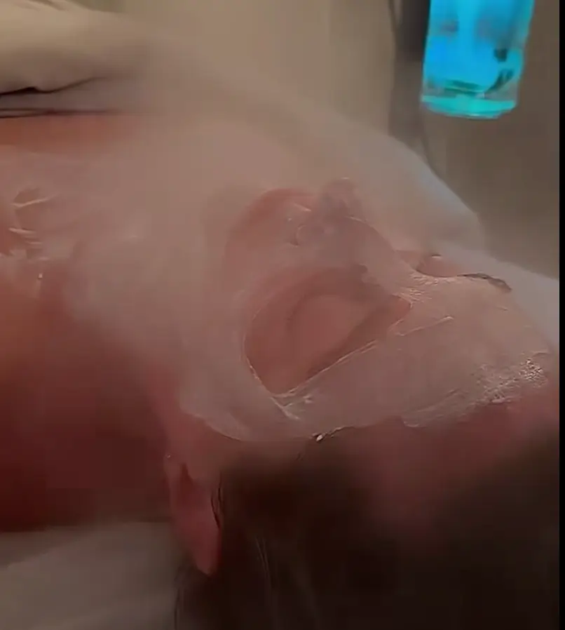 Person lying down with a thick white facial mask applied, eyes closed, receiving a spa or skincare treatment. - Jax Salon and Spa